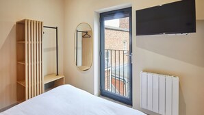 A bedroom with a bed, a wardrobe, a mirror, a radiator, and a window with a view of a building. - Host Stay No 33 (North Shields)