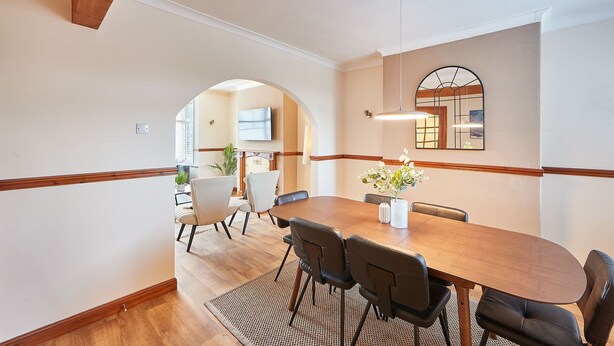 Un comedor con una mesa de madera, sillas negras, un tapete tejido y un espejo grande en la pared.