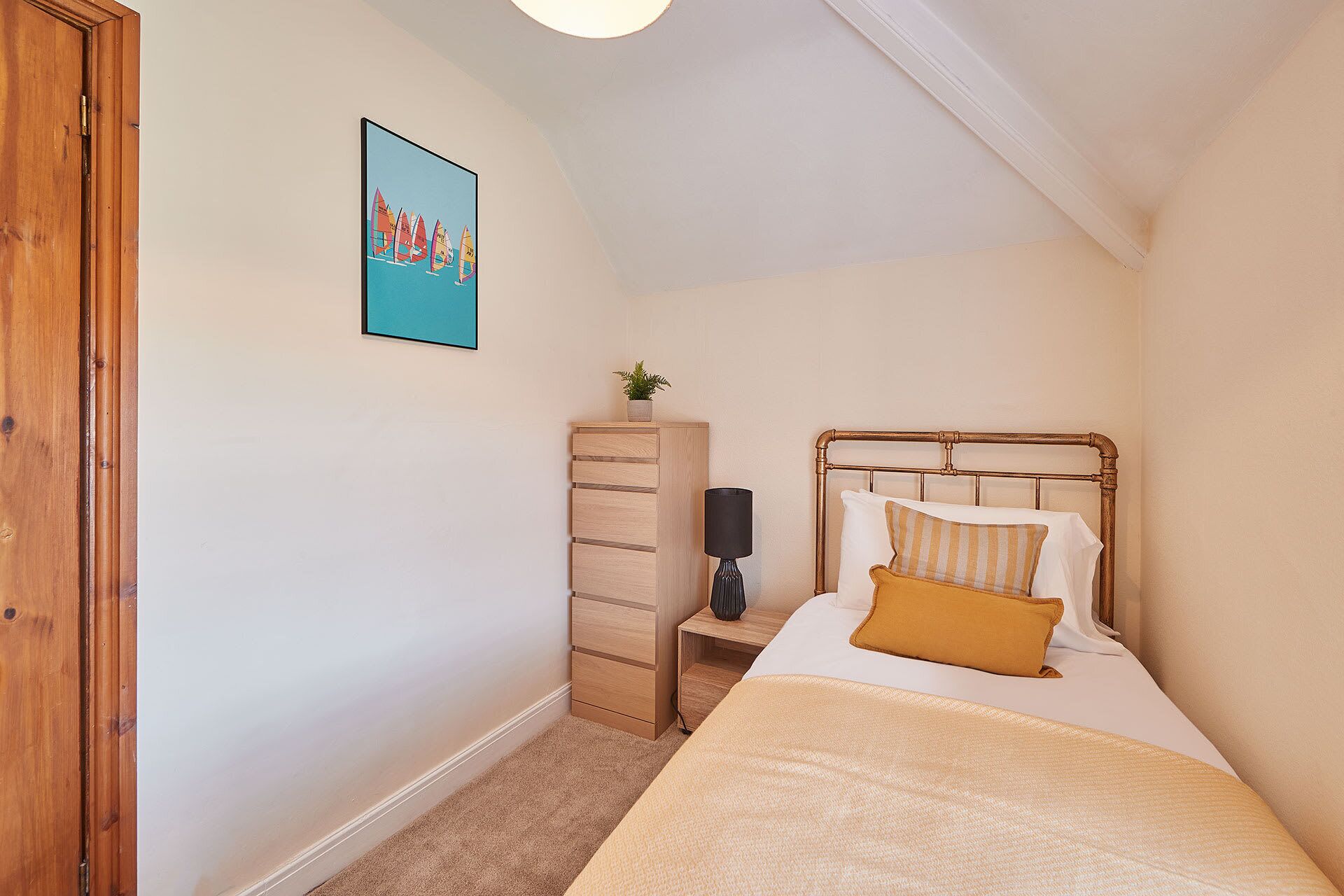 Une chambre à coucher comprenant un lit, une table de chevet, une lampe, une armoire en bois et un tableau encadré accroché au mur.