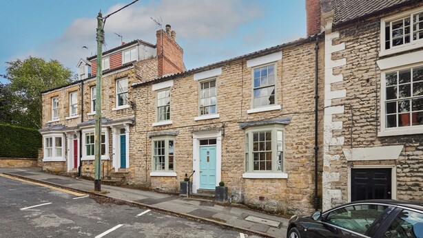 A row of stone buildings with traditional architecture, featuring multiple windows and doors, and a car parked on the street. - Host Stay Hall Garth (Pickering)