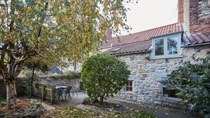 A stone building with a tiled roof, a stone wall, and a small garden area with chairs and a tree. - Host Stay Hall Garth (Pickering)