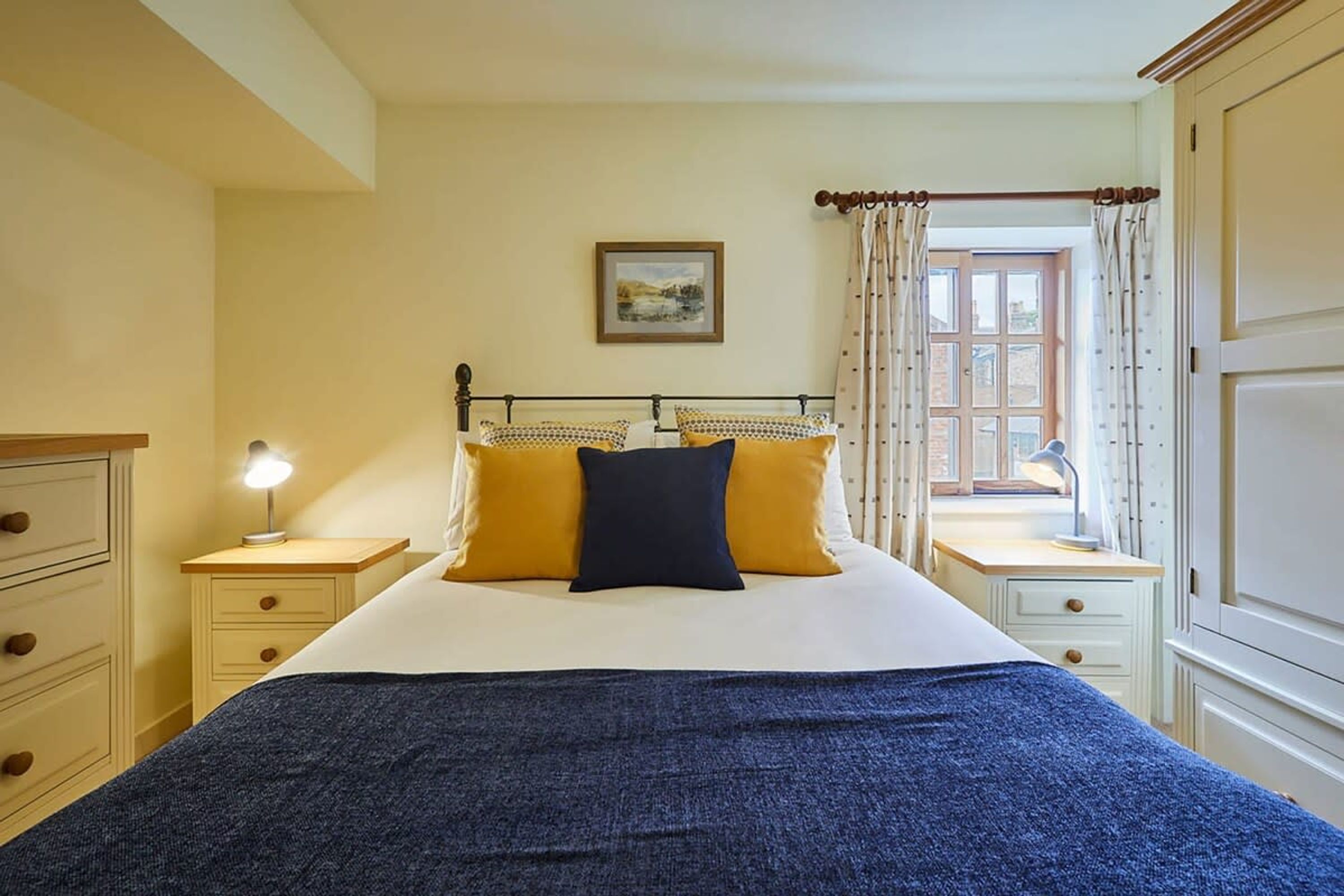 Ein Schlafzimmer mit einem Bett, zwei Nachttischen, einem Fenster mit Vorhängen und einem Bild an der Wand.