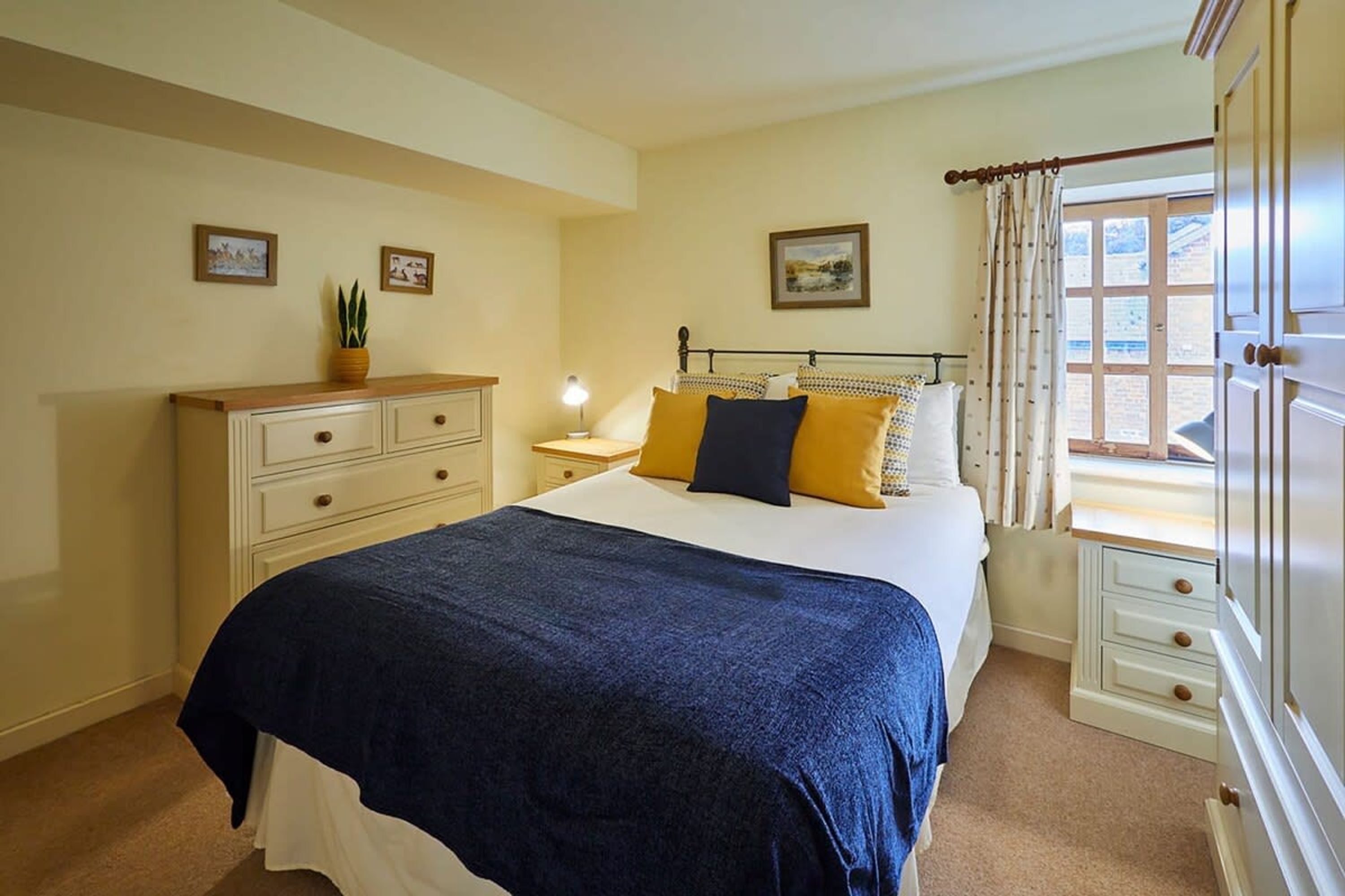 A bedroom with a bed, a nightstand, a dresser, and a window with curtains.