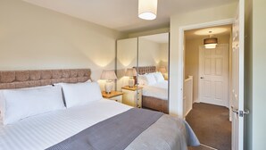 Une chambre à coucher bien aménagée, avec un grand lit, des lampes de chevet, un miroir et une porte donnant sur une autre pièce.