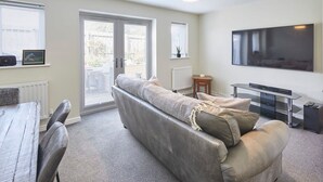 Un salon moderne avec un canapé gris, une table à manger avec des chaises, un téléviseur et un radiateur.
