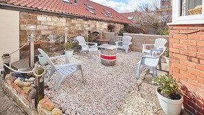A patio area with white plastic chairs, a table, and a decorative stone planter. - Host Stay Mumbles Cottage (Whitby)