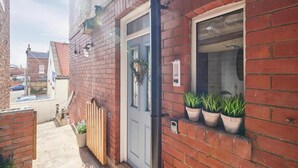 A narrow alleyway with a red brick building, a blue door, and potted plants on the windowsill. - Host Stay Mumbles Cottage (Whitby)
