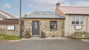 Un bâtiment en pierre avec une porte noire, une plaque portant l’inscription « Le vieux salon de coiffure de la prison », et une petite fenêtre.