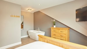 Une chambre moderne avec un grand lit, une baignoire intégrée, une commode en bois et un téléviseur à écran plat fixé au mur.