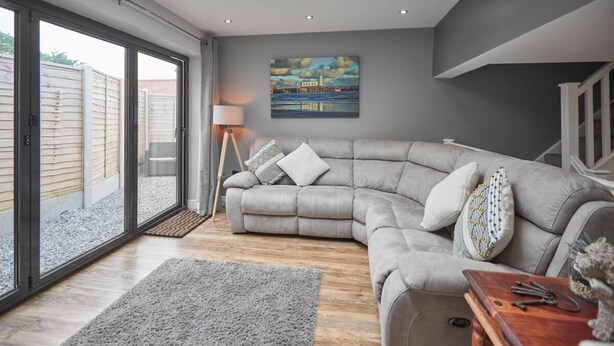 Un salon moderne avec un canapé d’angle gris, une table basse en bois et un tableau accroché au mur.