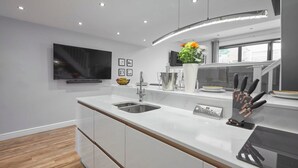 Une cuisine moderne dotée d’un grand îlot central, d’appareils électroménagers en acier inoxydable et d’un téléviseur à écran plat fixé au mur.