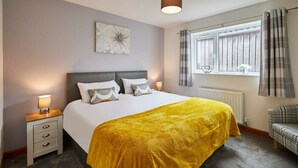 A bedroom with a bed, bedside lamps, a window with curtains, a radiator, and a wall-mounted artwork. - Host Stay Dove Cottage (Pickering)