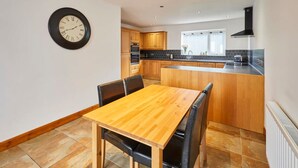 A modern kitchen with wooden cabinets, a central island, and a dining area with a wooden table and chairs. - Host Stay Dove Cottage (Pickering)