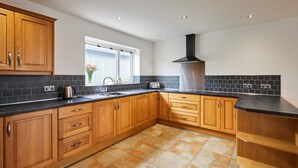 A kitchen with wooden cabinets, a black countertop, and a tiled floor. - Host Stay Dove Cottage (Pickering)
