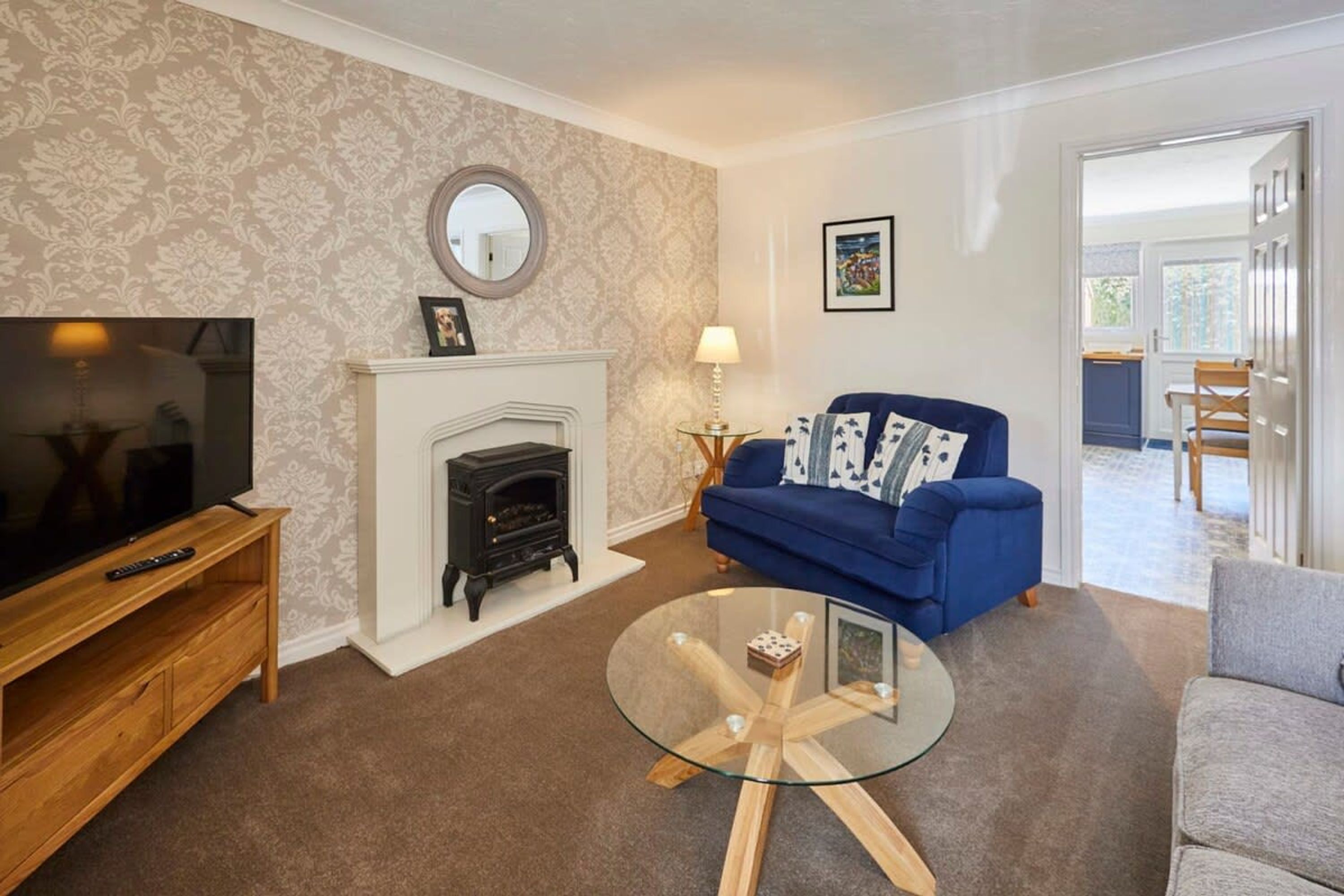 A living room with a television, fireplace, blue sofa, and glass coffee table.