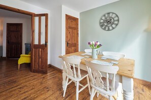 A dining area with a wooden table, white chairs, and a wall clock.