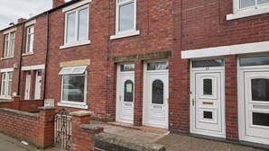 A row of red brick terraced houses with white doors and windows, numbered 17 to 19. - Host Stay Inness House (Bedlington)