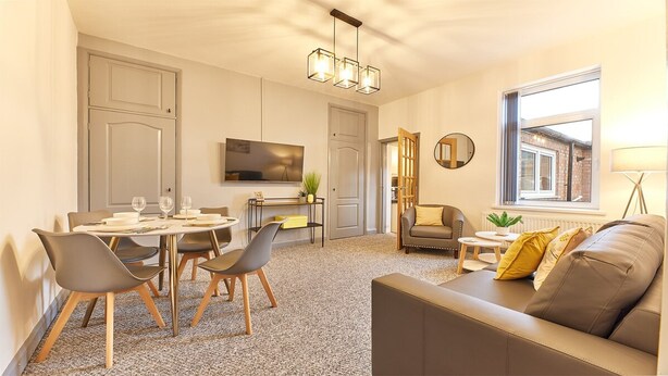 A modern living room with a sofa, a dining table set for four, a TV mounted on the wall, and a window with a view. - Host Stay Inness House (Bedlington)
