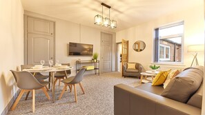 A modern living room with a sofa, a dining table set for four, a TV mounted on the wall, and a window with a view. - Host Stay Inness House (Bedlington)