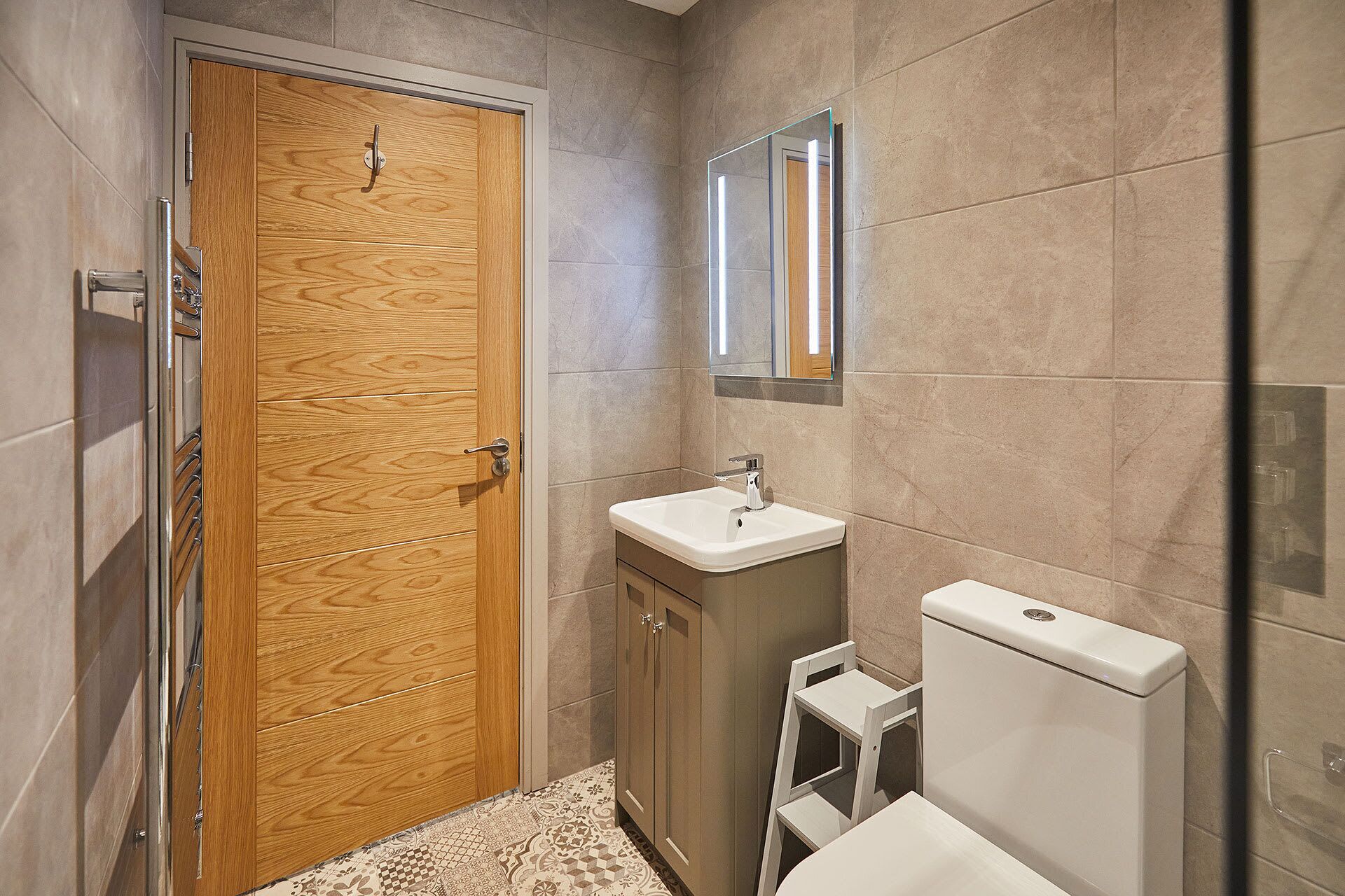 A bathroom with a wooden door, a white sink, a mirror, and a toilet.