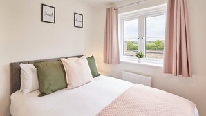 A neatly made bed with a white and pink blanket, a gray headboard, and two pillows (one green and one white). - Host Stay Cayton Bay Cottage (Scarborough)