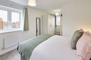A bedroom with a large bed, a window with curtains, a radiator, and a wardrobe.
