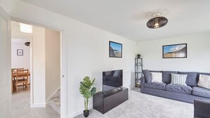 A modern living room with a grey sofa, a flat-screen TV, and a staircase leading to another room. - Host Stay Cayton Bay Cottage (Scarborough)