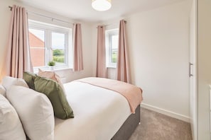 A bedroom with a bed, two windows, and a view of a brick building outside.