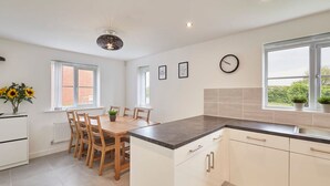 A modern kitchen with white cabinets, a black countertop, and a dining area with wooden chairs and a table. - Host Stay Cayton Bay Cottage (Scarborough)