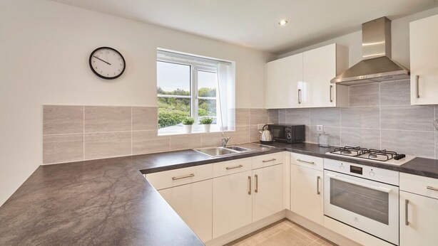 A modern kitchen with white cabinets, a black countertop, a stove, and a microwave. - Host Stay Cayton Bay Cottage (Scarborough)