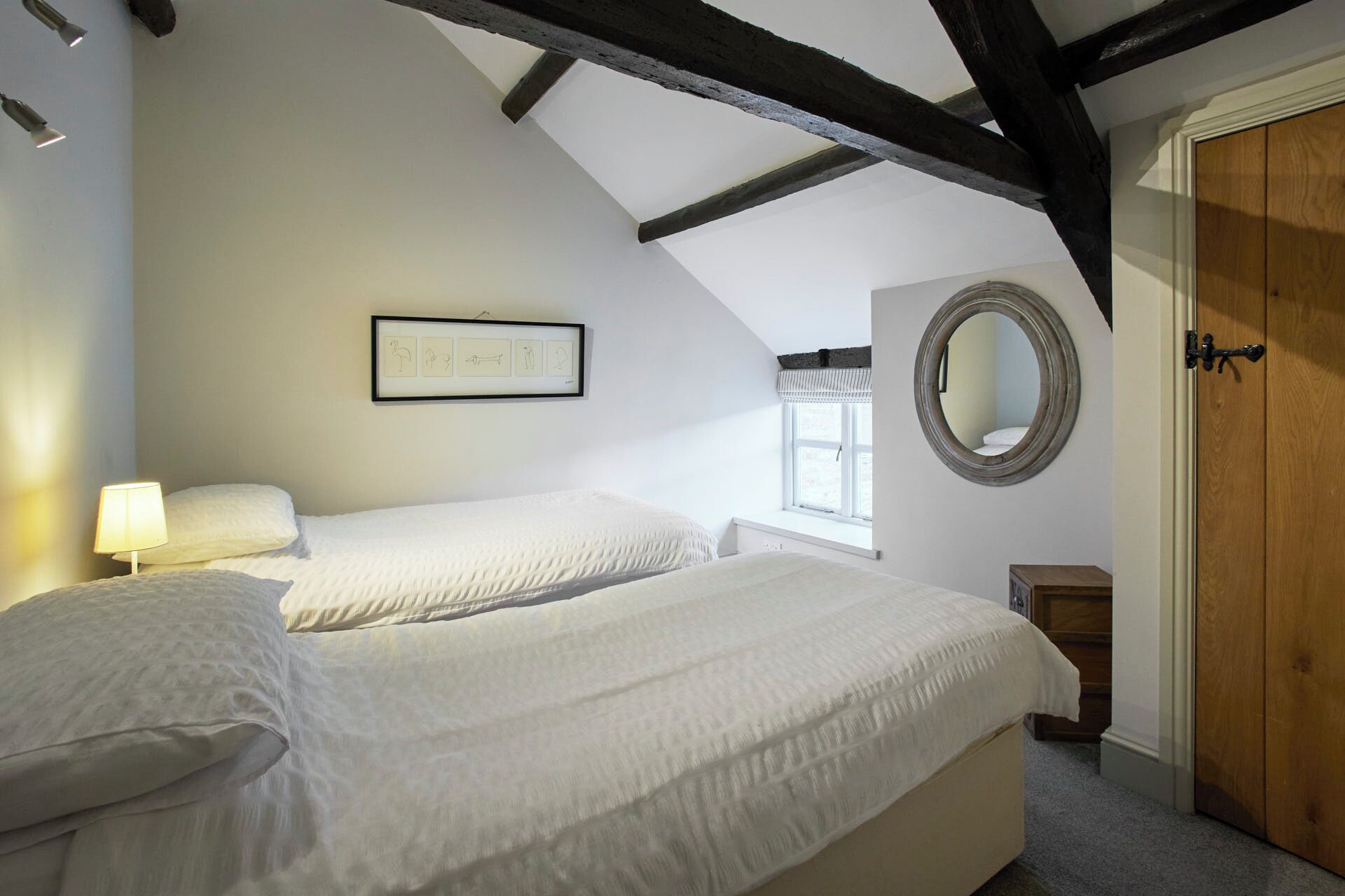 A bedroom with two beds, a framed picture on the wall, a window, and a wooden door.