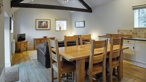 Un coin repas avec une table et des chaises en bois, un téléviseur posé sur un meuble en bois, un canapé et un coin cuisine avec une fenêtre.