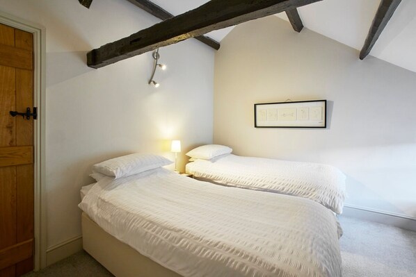 Une chambre avec deux lits, une porte en bois et un tableau encadré au mur.