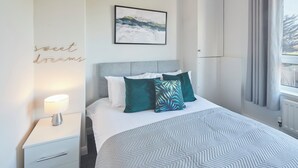 Une chambre d’hôtel bien rangée, avec un lit, une table de chevet dotée d’une lampe, une œuvre d’art accrochée au mur et une fenêtre avec des rideaux.
