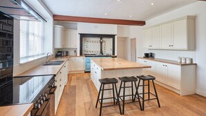 A modern kitchen with a central island, bar stools, and a built-in oven. - Host Stay Silton Hall (Thirsk)