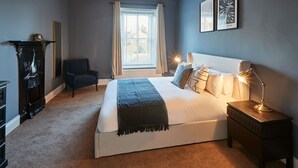 A bedroom with a large bed, bedside lamps, a chair, a dresser, and a window with curtains. - Host Stay Silton Hall (Thirsk)
