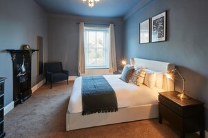 A bedroom with a large bed, bedside lamps, a chair, a dresser, and a window with curtains.