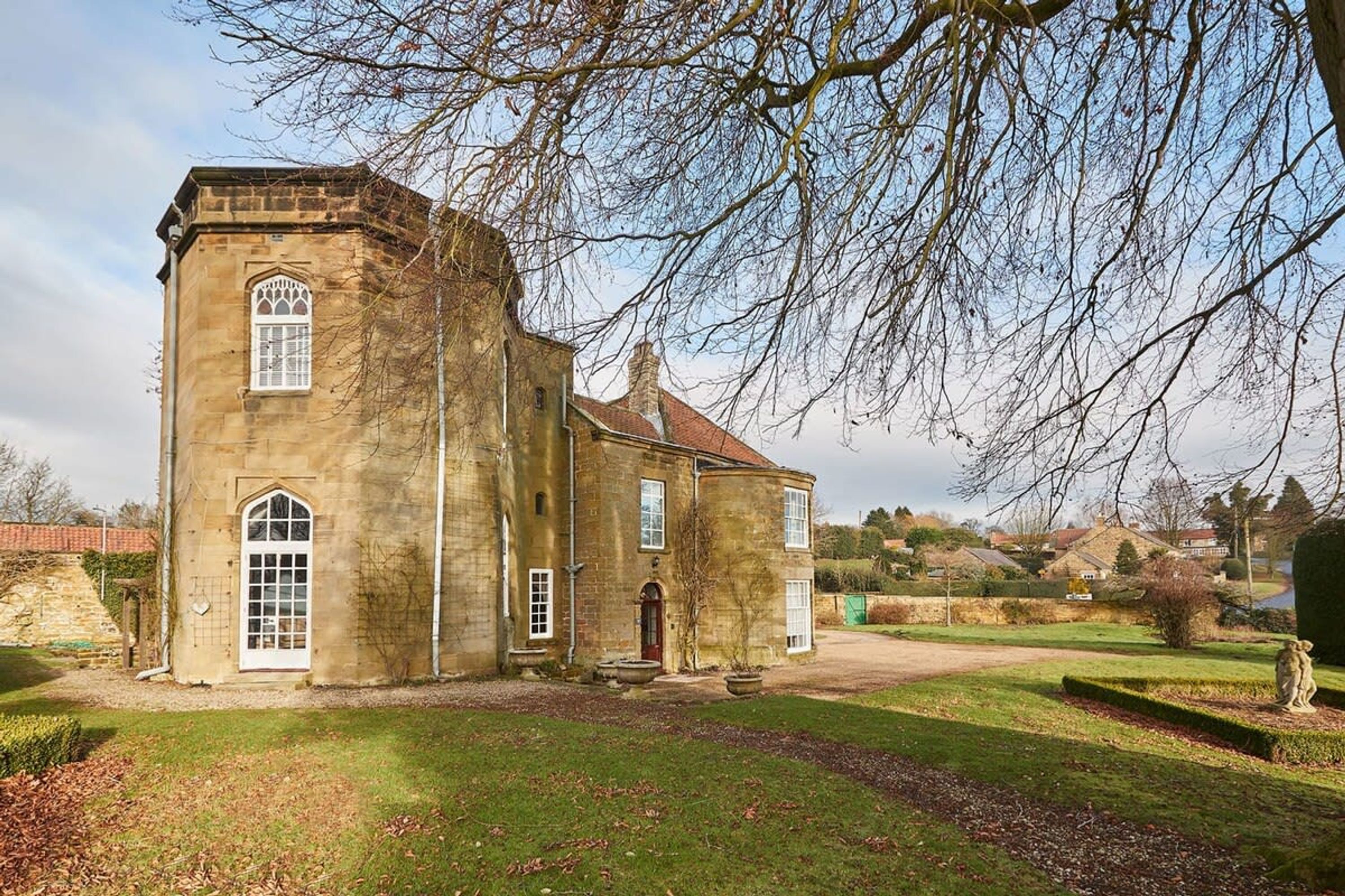 A historic stone building with a prominent tower, large windows, and a well-maintained lawn.