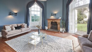 A living room with a fireplace, a sofa, a coffee table, and a large window with curtains. - Host Stay Silton Hall (Thirsk)