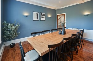 A dining room with a wooden table and chairs, blue walls, and wall-mounted lights.