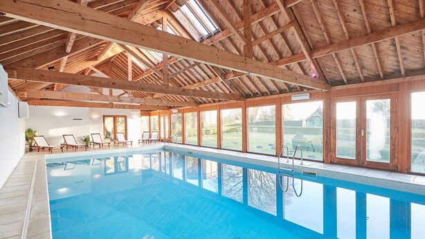 An indoor swimming pool with wooden beams, clear glass windows, and lounge chairs. - Host Stay Silton Hall (Thirsk)