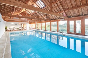 An indoor swimming pool with wooden beams, clear glass windows, and lounge chairs.