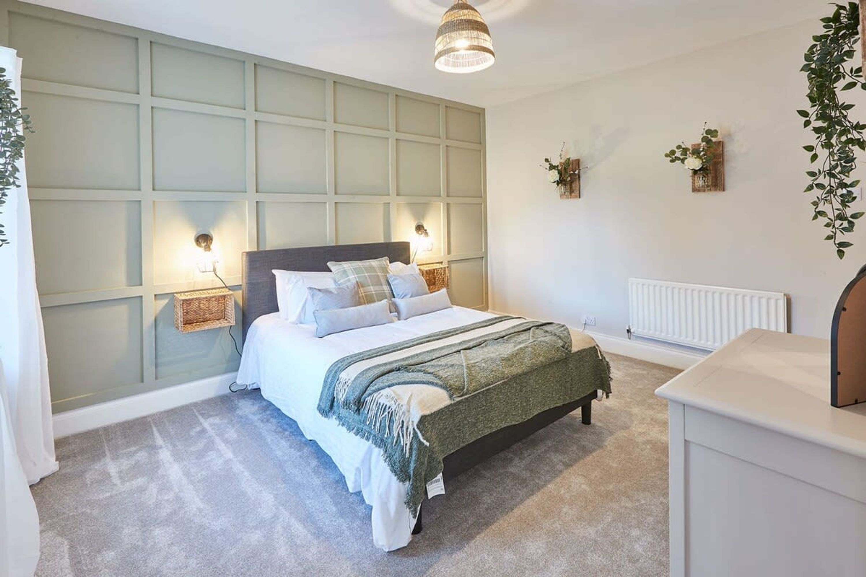 A bedroom with a bed, bedside lamps, a radiator, and a hanging plant.