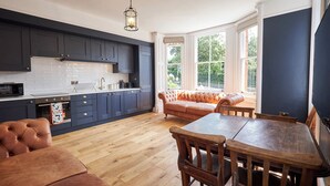 A modern kitchen with dark cabinets, a wooden dining table, and a cozy seating area by large windows.