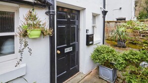A black door with the number 14, a green hanging plant, and a mailbox on a white wall. - Host Stay Scoresby Place (Whitby)