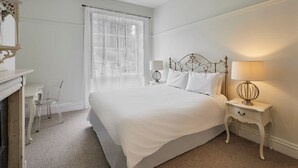 A bedroom with a large bed, a bedside table with a lamp, a small table with chairs, and a window with sheer curtains. - Host Stay Scoresby Place (Whitby)