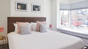A large bed with a wooden headboard, white bedding, and multiple pillows. There are two framed pictures on the wall above the bed. - Host Stay Upleatham Street (Saltburn-by-the-Sea)