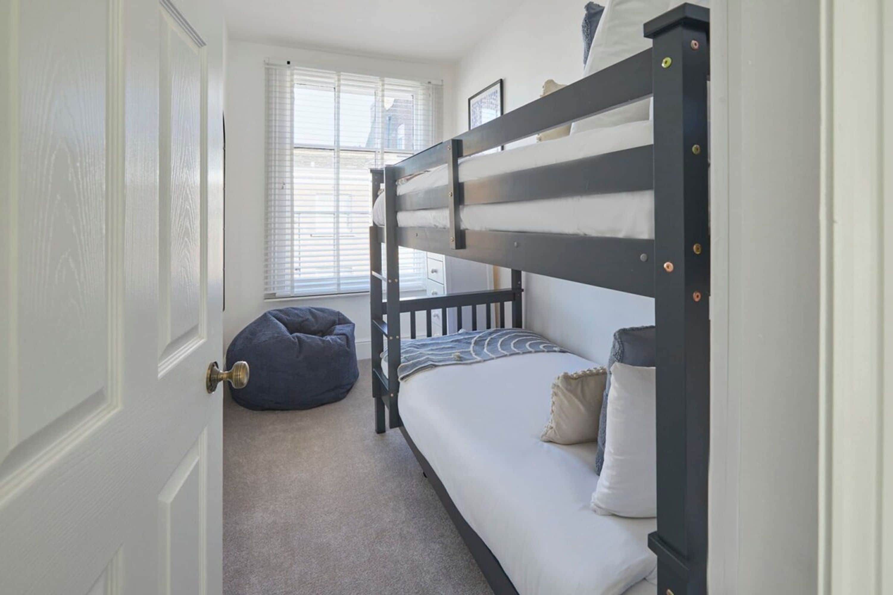 A bunk bed room with a door, a window, and a bean bag chair.