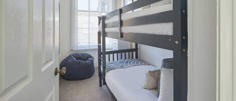 A bunk bed room with a door, a window, and a bean bag chair.