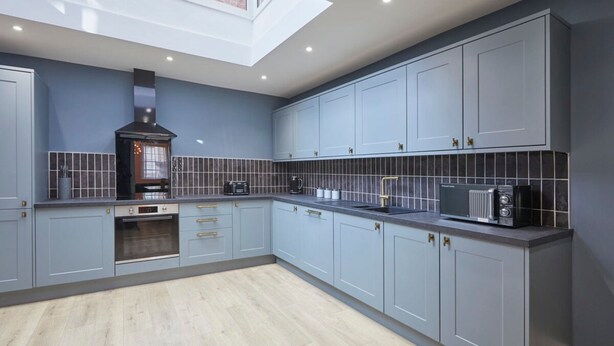 A modern kitchen with grey cabinets, a built-in oven, and a black range hood. - Host Stay Castle View (Scarborough)